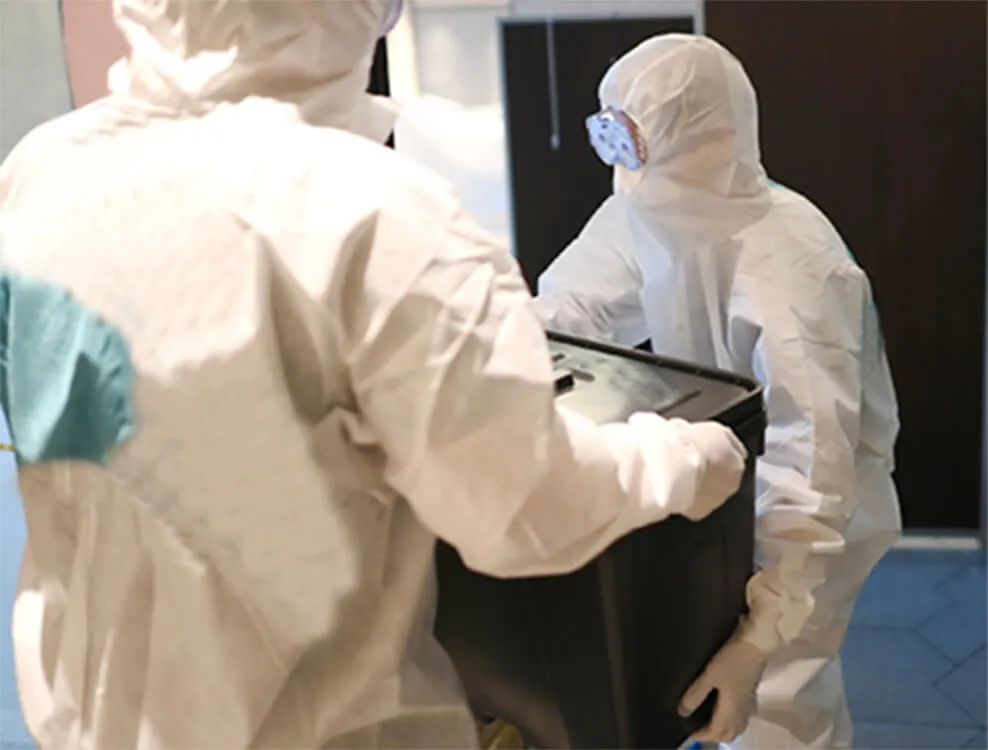 白い防護服とゴーグルをした業者が家具を運ぶ様子