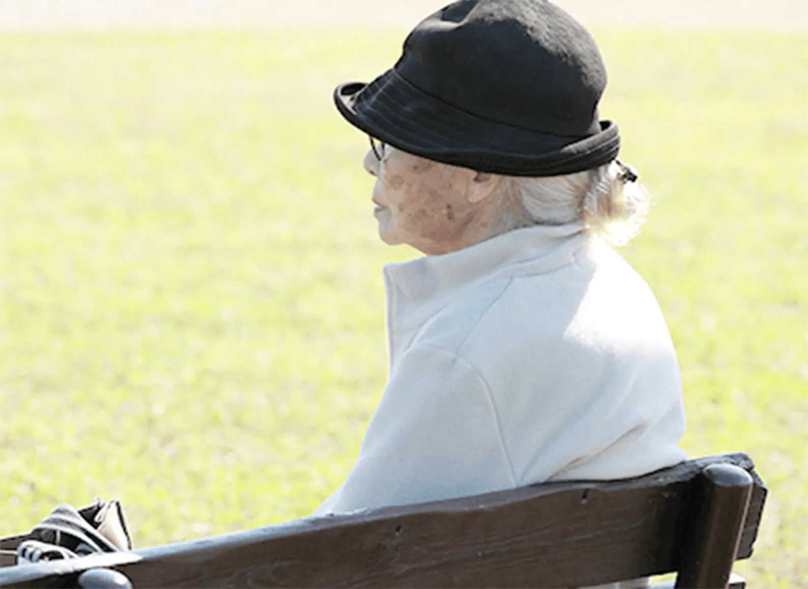 芝生の床に設置してあるベンチに座って前を向く帽子を被った老人